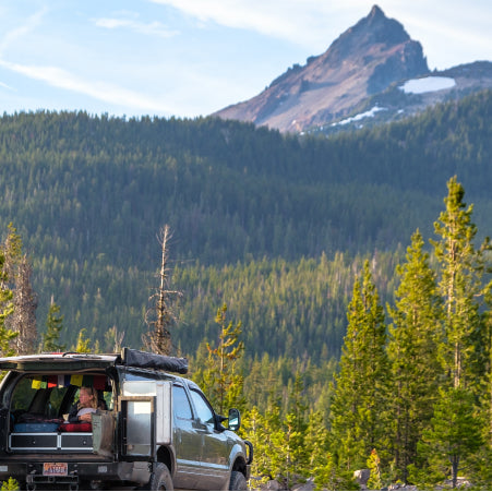 SUV in forest with mountain peak in background