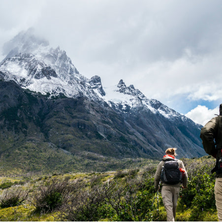 man and woman hiking near mountains wearing backpacks