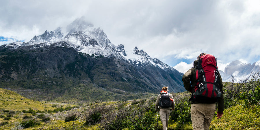 man and woman hiking near mountains wearing backpacks